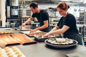 a man and woman in a commercial kitchen creating platters