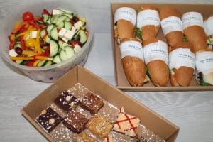 A lunch package featuring fresh vegetable salad, baguette sandwiches, and a dessert box of assorted brownies.