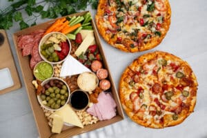 Platter filled with cold meats, vegetables, and antipasti, and two pizzas