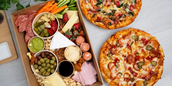 Platter filled with cold meats, vegetables, and antipasti, and two pizzas