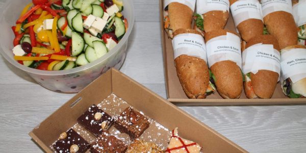A lunch package featuring fresh vegetable salad, baguette sandwiches, and a dessert box of assorted brownies.
