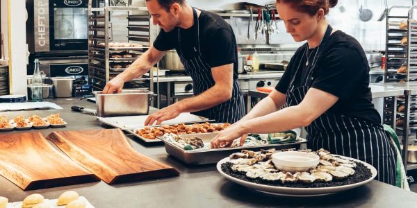 a man and woman in a commercial kitchen creating platters
